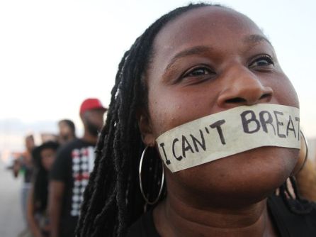 A Black woman with tape over her mouth on which the words &quot;I can't breathe&quot; are written